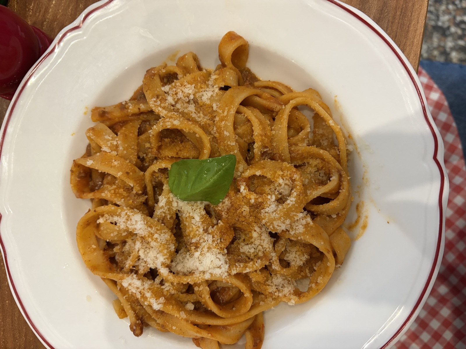 A bowl of tagliatelle with ragù, parmesan and a single basil leaf