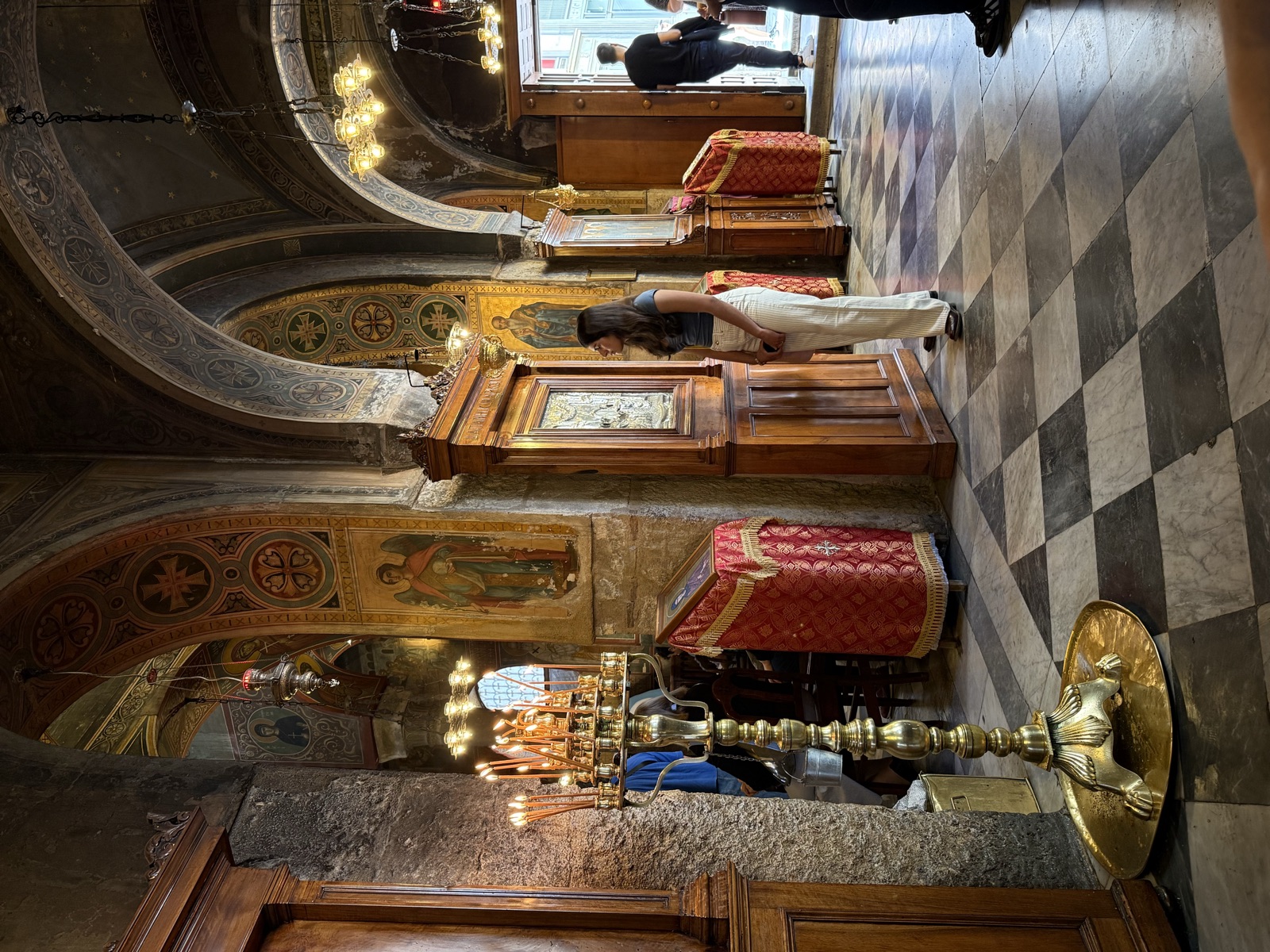 The interior of a church in Greece, candles burning beneath frescoed arches